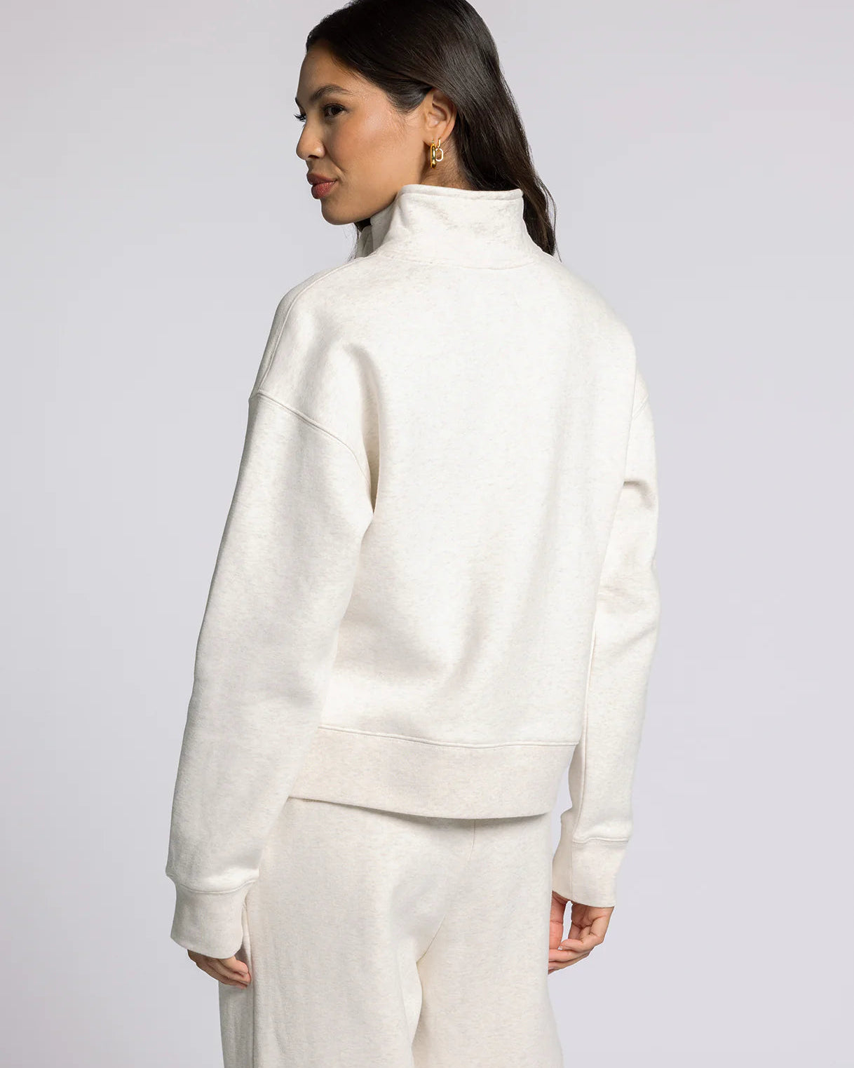 Woman wearing a white high-neck sweater and pants on a light gray background