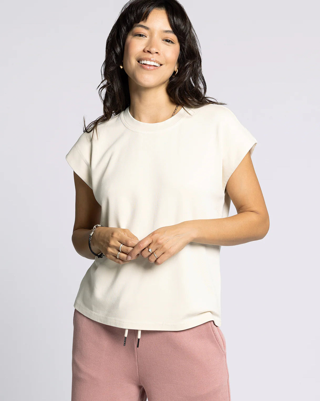 Woman wearing a white t-shirt and pink pants against a plain background