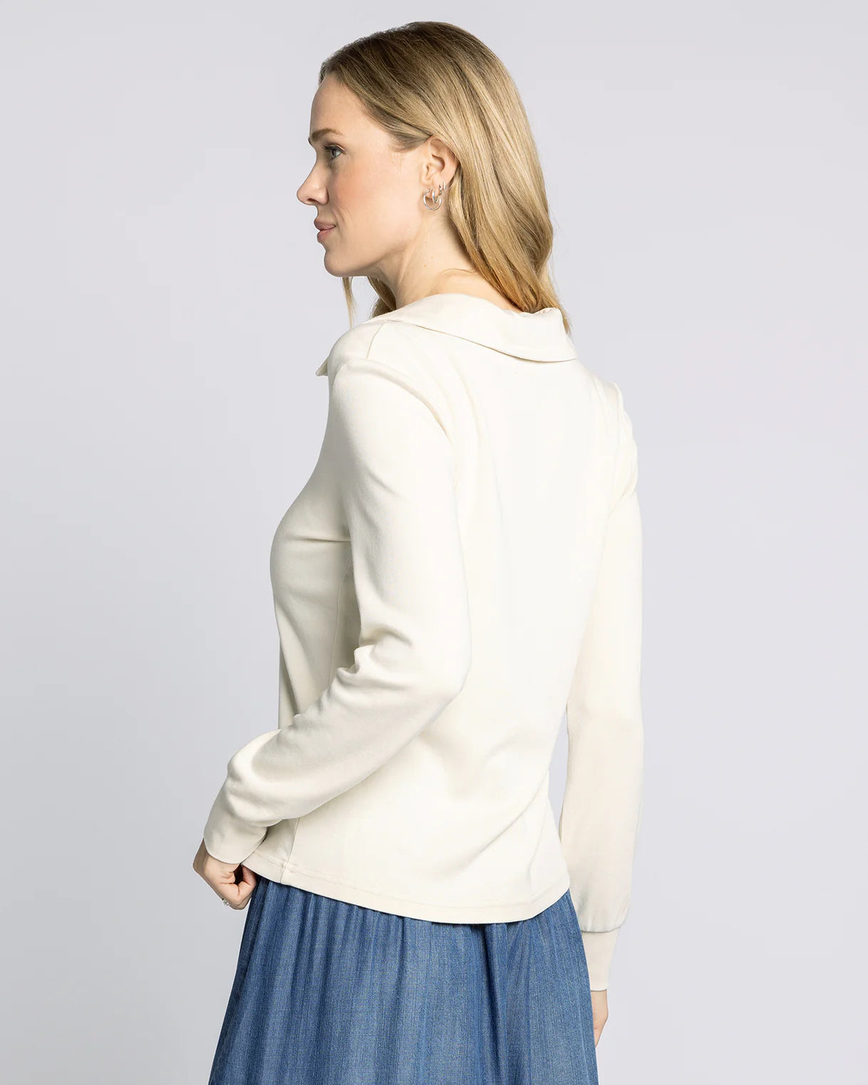 Woman wearing a white jacket and blue skirt on a plain background