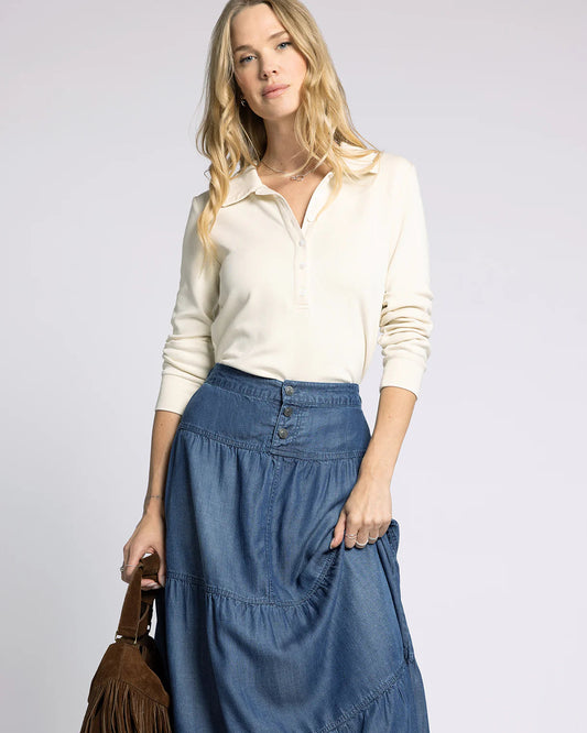 Woman wearing a white shirt and blue denim skirt holding a brown handbag on a light gray background