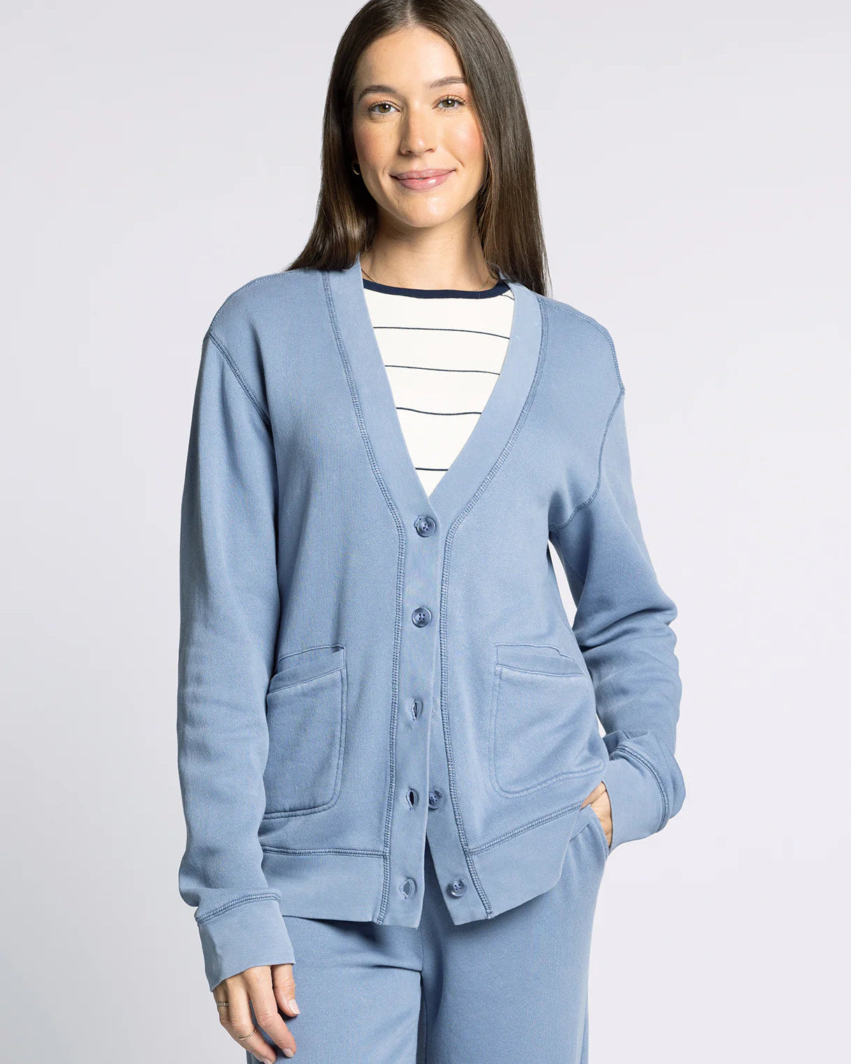 Woman wearing a light blue cardigan over a striped shirt on a plain background