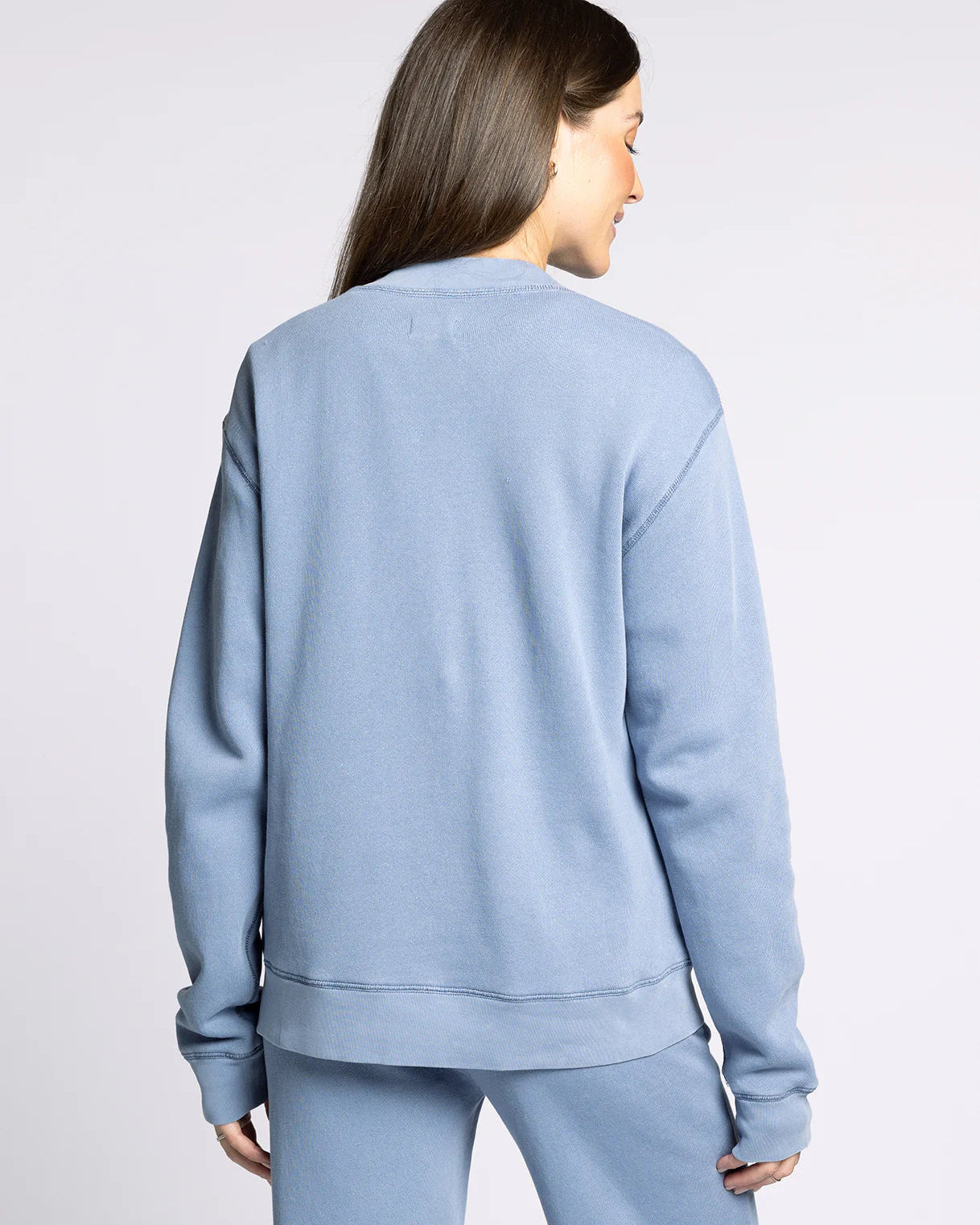 Woman wearing a light blue sweatshirt and pants on a plain background
