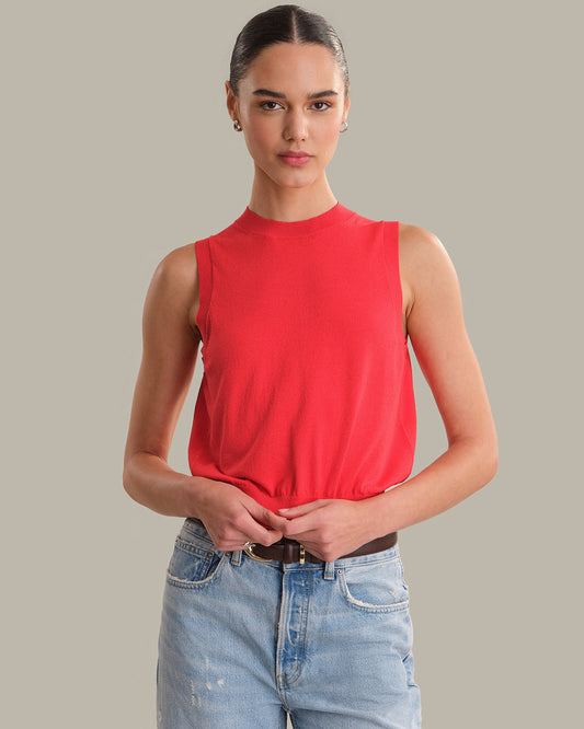 Woman wearing a red sleeveless top and light blue jeans against a gray background