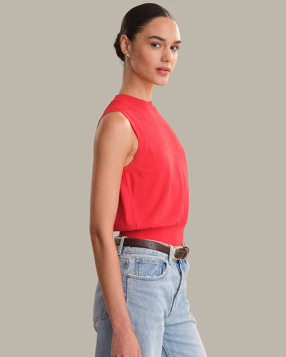 Woman wearing a red sleeveless top and light blue jeans against a gray background