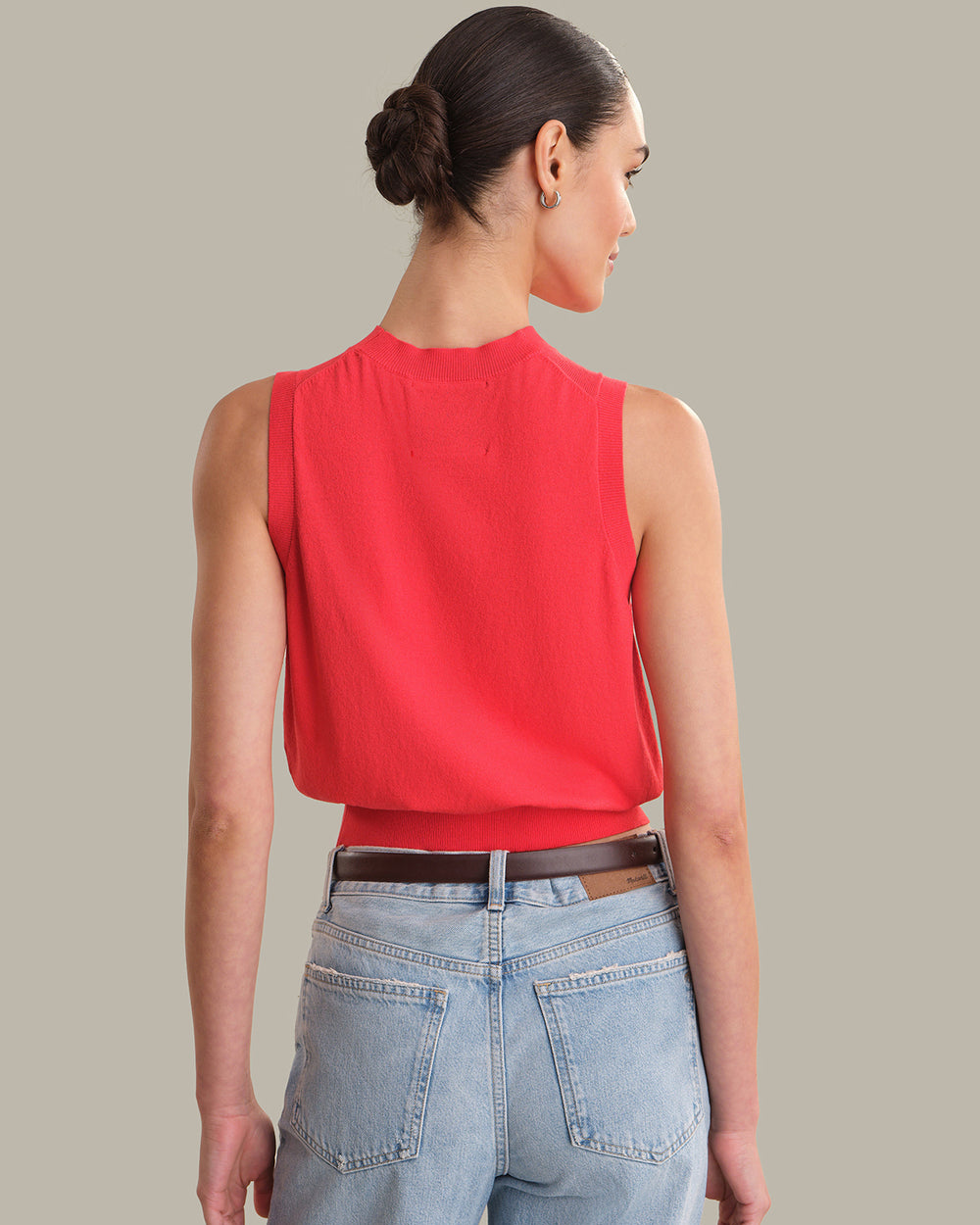 Woman wearing a red sleeveless top and light blue jeans on a neutral background