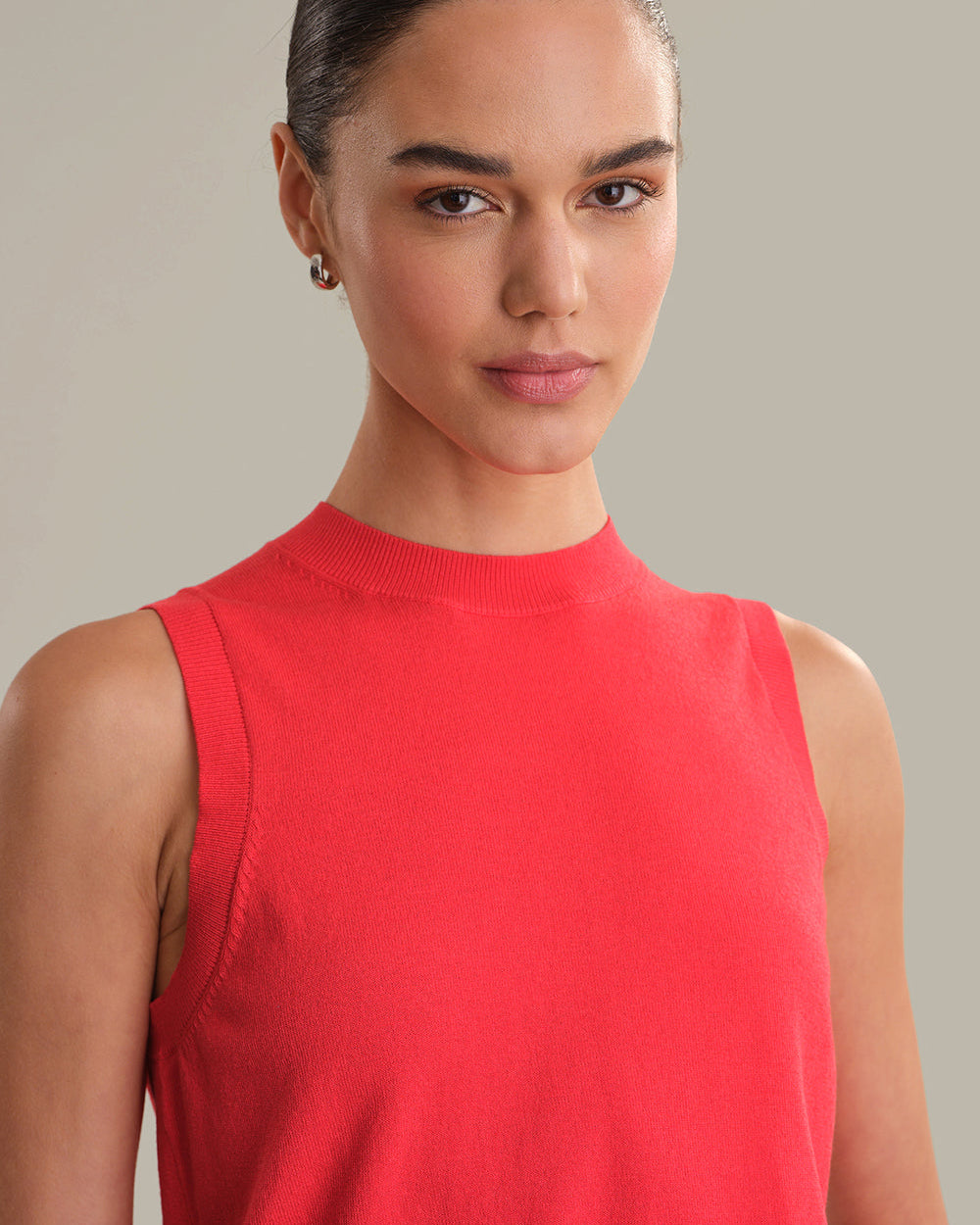 Woman wearing a red sleeveless top against a neutral background
