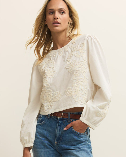 Woman wearing a white blouse with lace details and blue jeans on a plain background