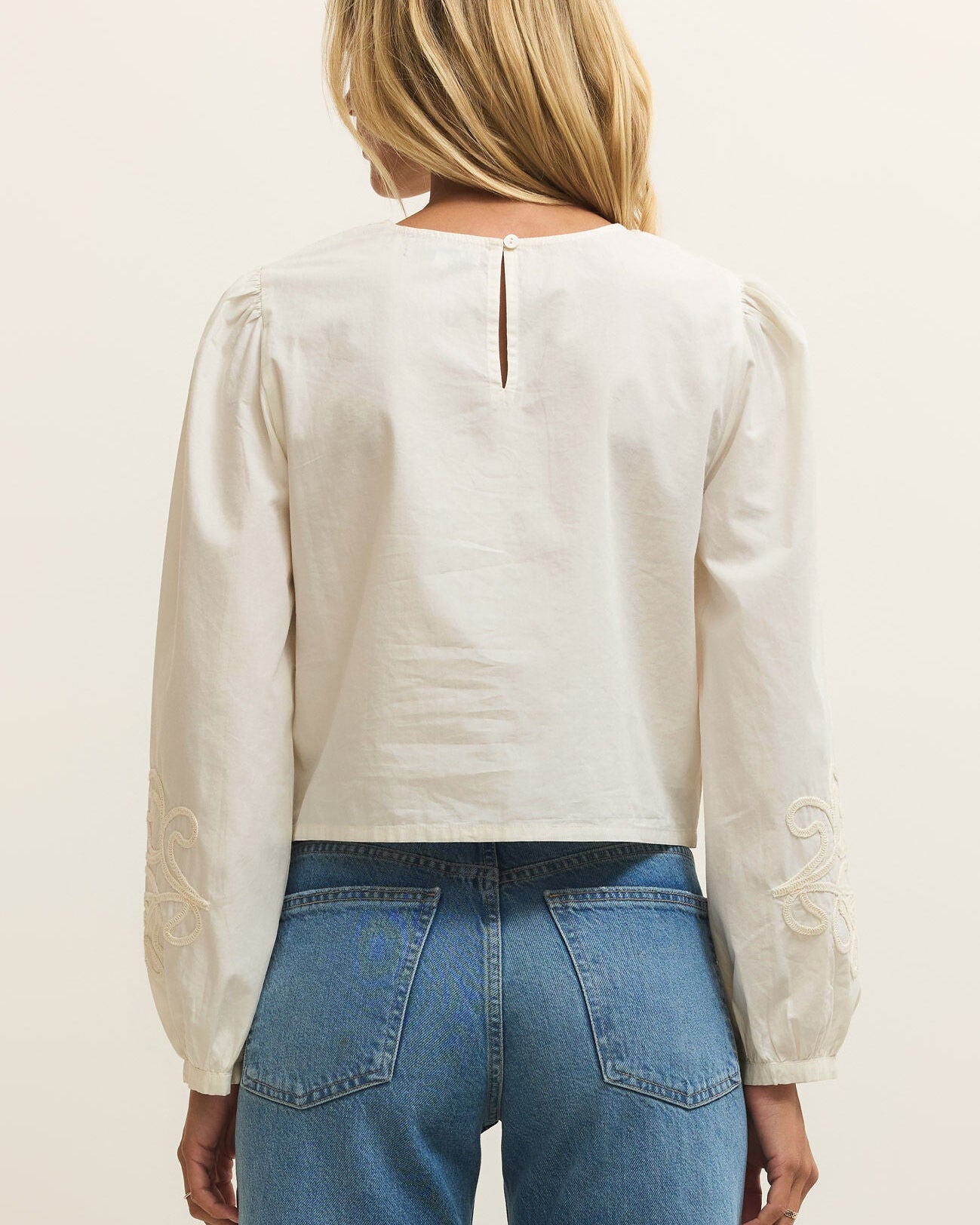 Person wearing a white blouse and blue jeans on a plain background