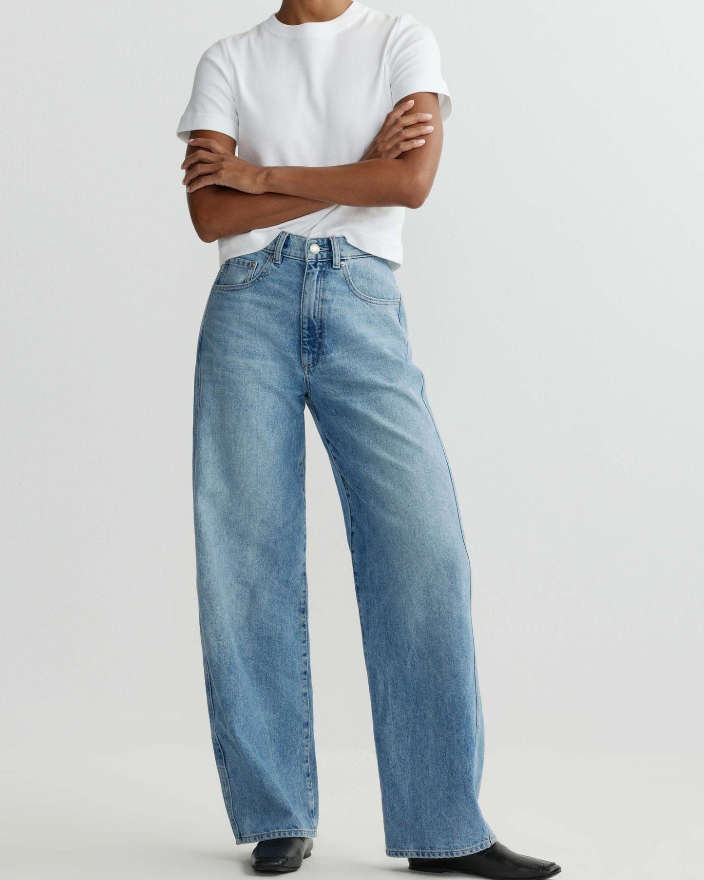 Person wearing light blue jeans and a white t-shirt on a plain background
