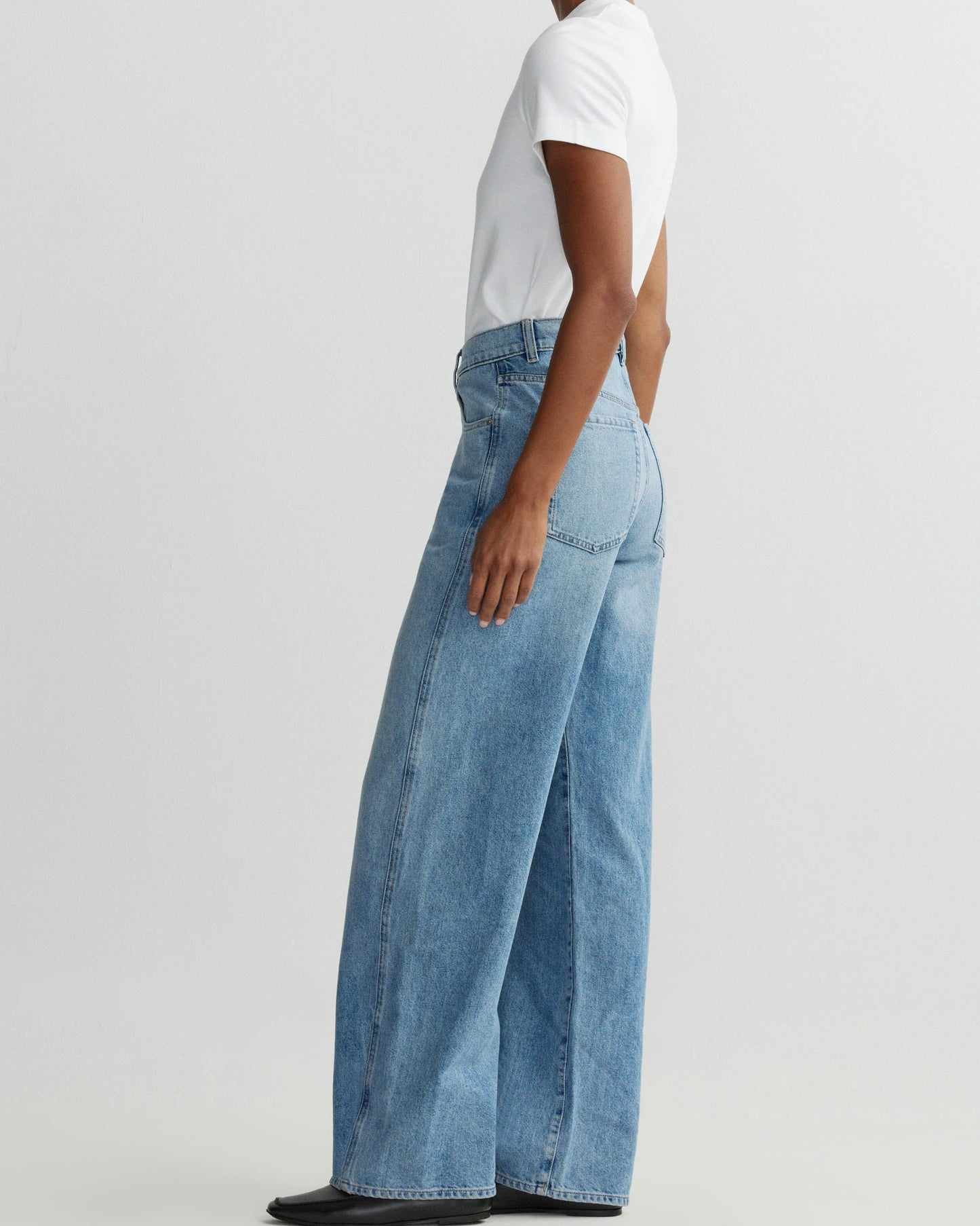 Person wearing light blue jeans and a white shirt on a plain background