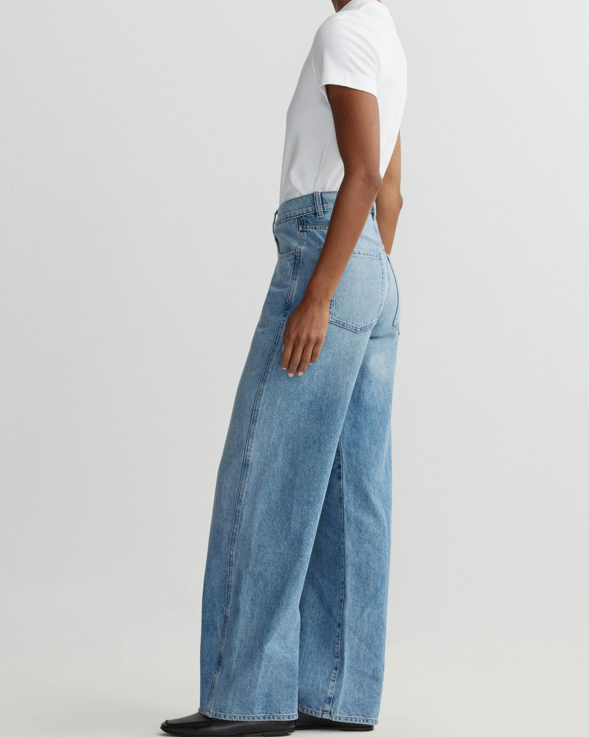 Person wearing light blue jeans and a white shirt on a plain background