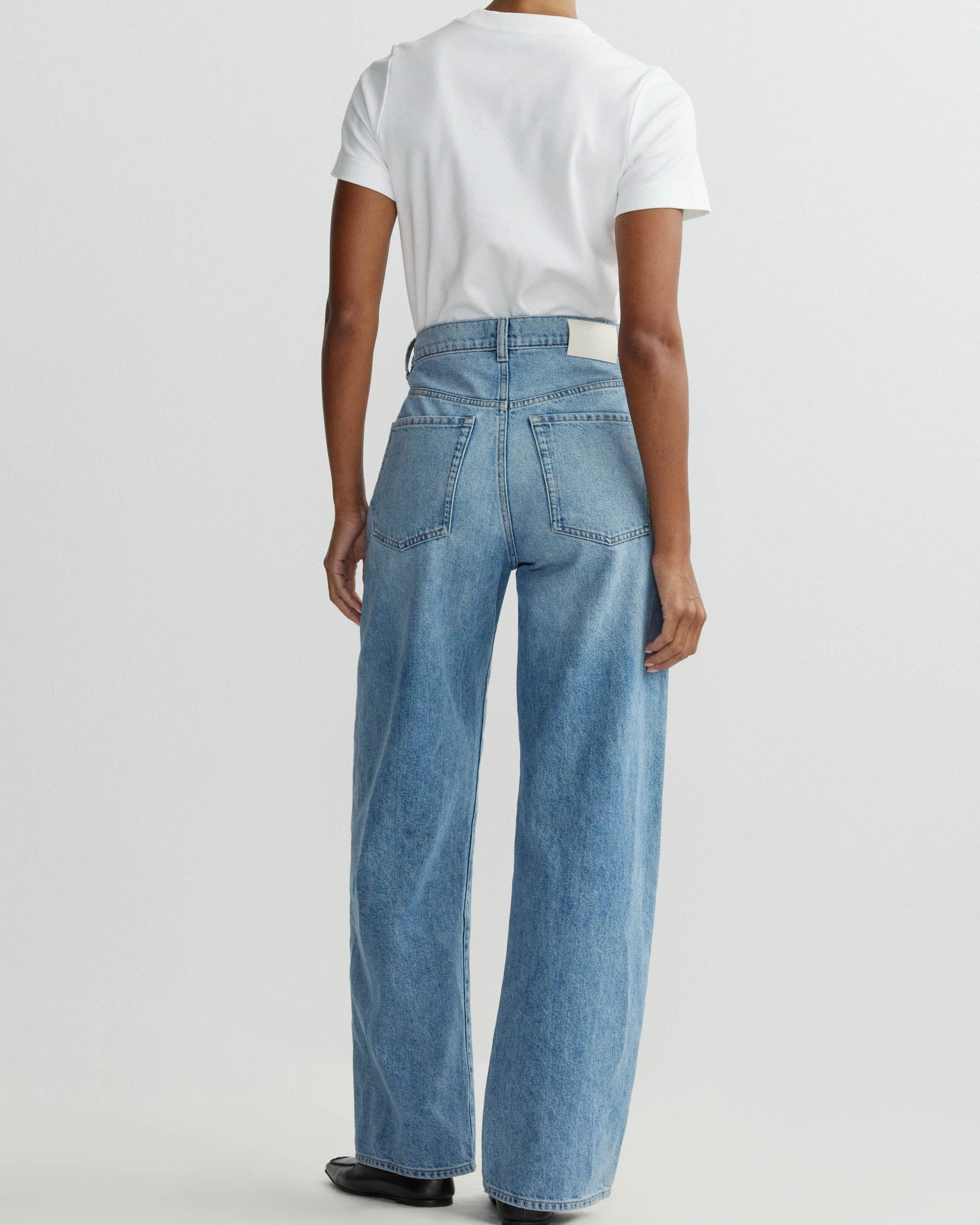 Person wearing a white t-shirt and blue jeans on a plain background