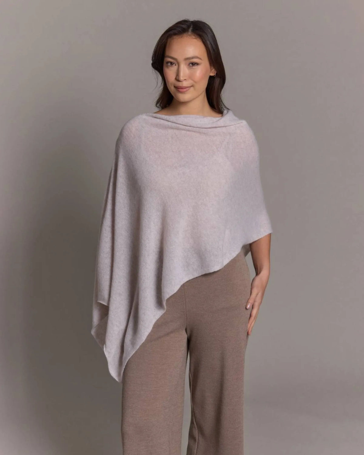 Woman wearing a light gray poncho over a matching outfit against a plain background