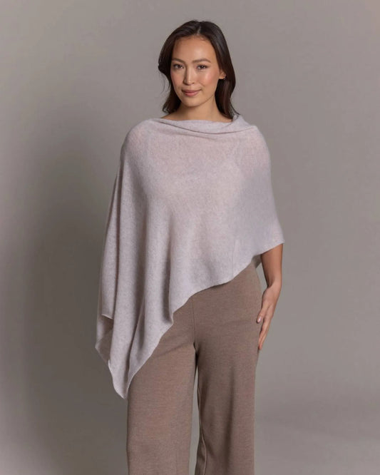 Woman wearing a light gray poncho over a matching outfit against a plain background