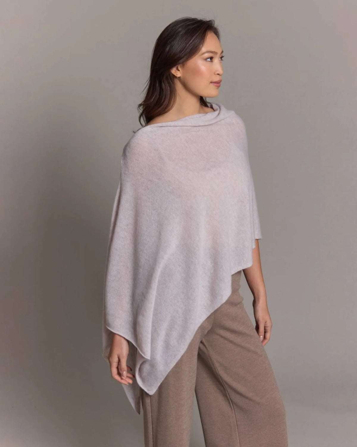 Woman wearing a light gray poncho against a plain background