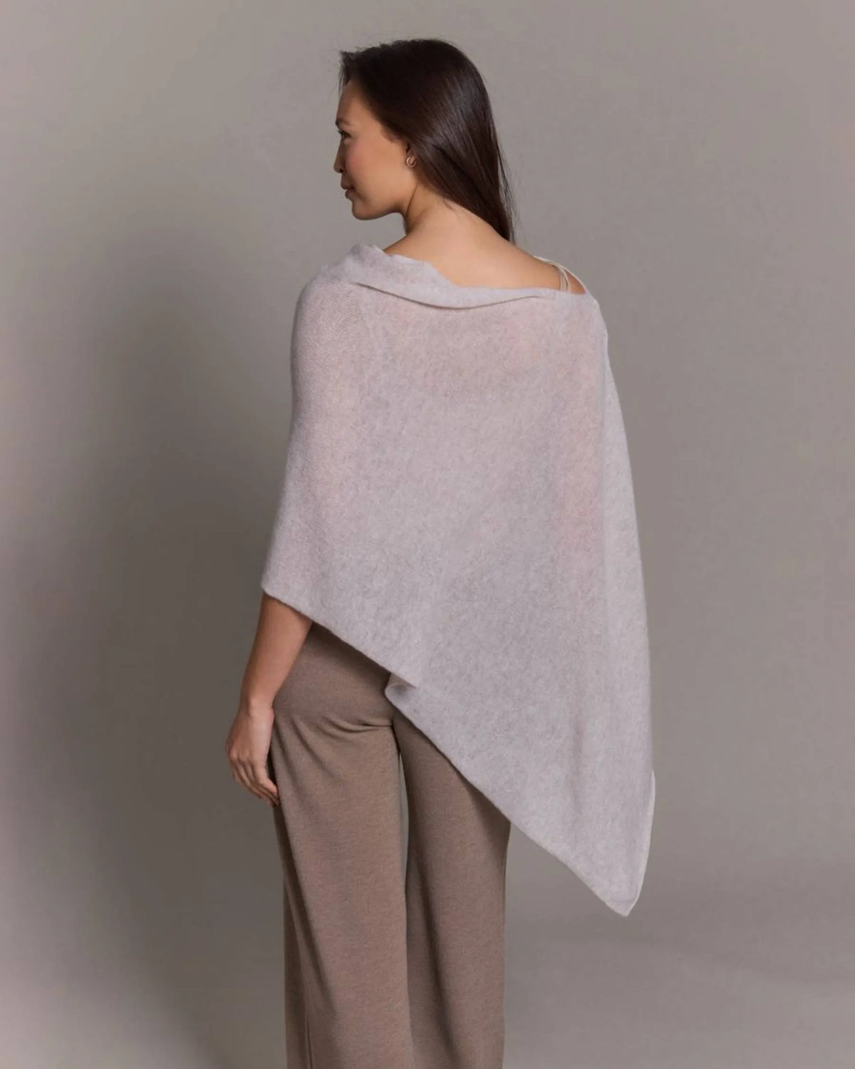 Woman wearing a light gray poncho against a plain background