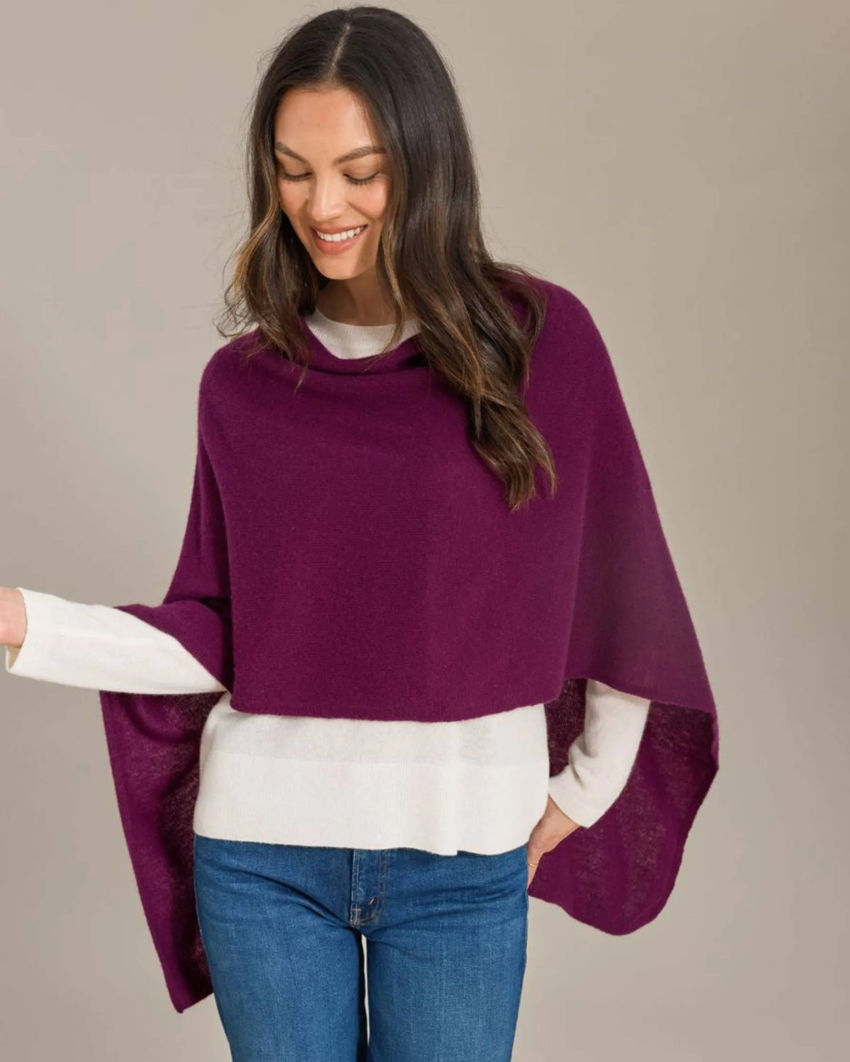Woman wearing a purple poncho over a white shirt and blue jeans on a beige background