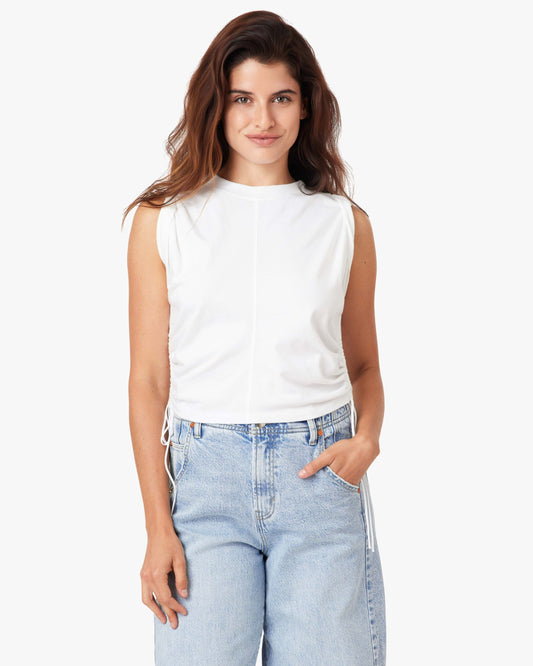 Woman wearing a white sleeveless top and light blue jeans on a white background