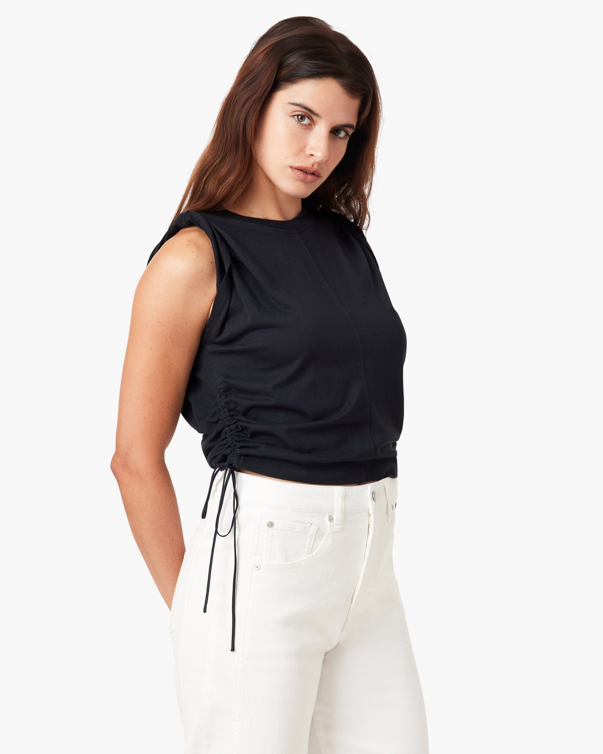 Woman wearing a black sleeveless top and white pants on a white background