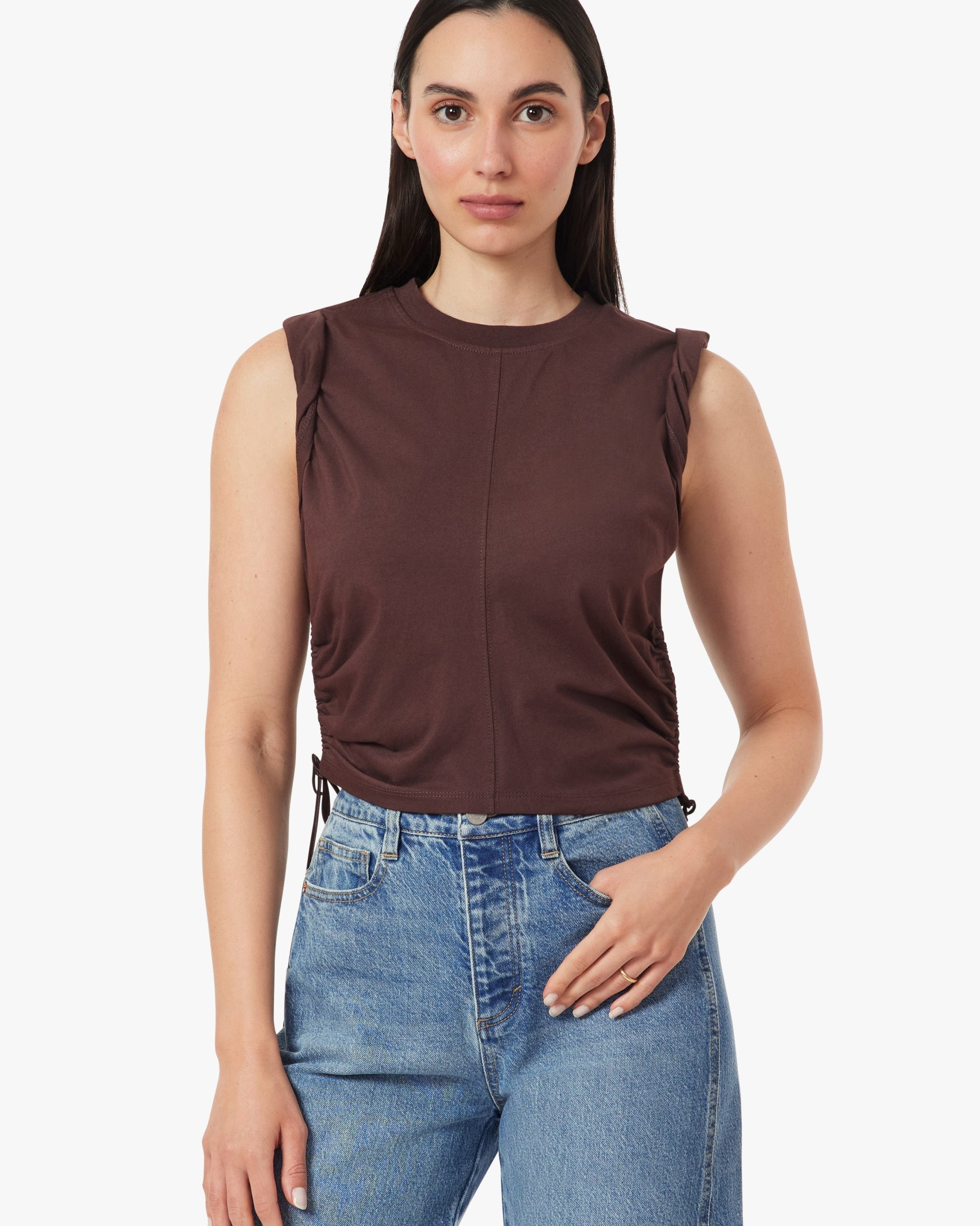 Woman wearing a brown sleeveless top and blue jeans on a white background