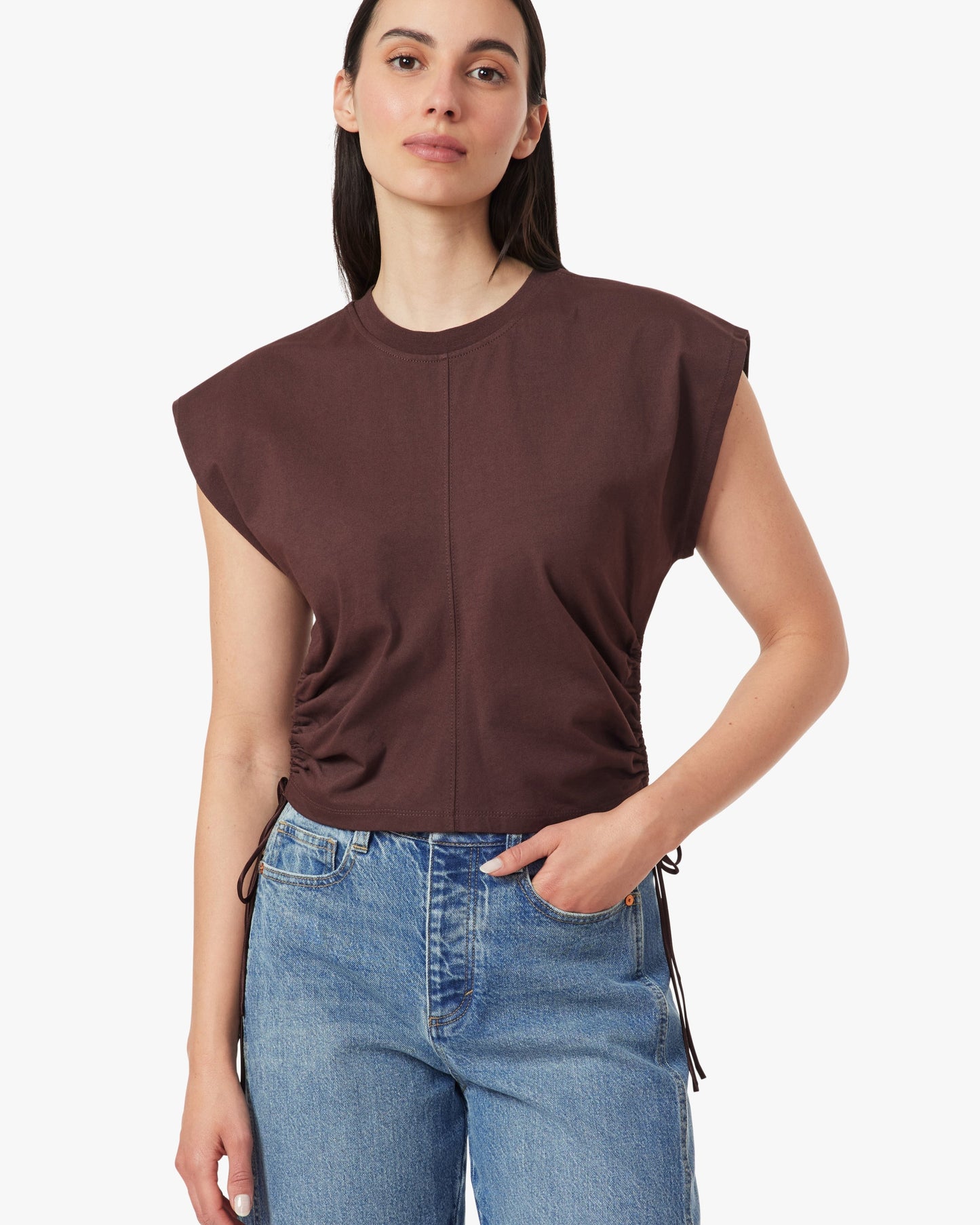 Woman wearing a brown sleeveless top and blue jeans on a white background