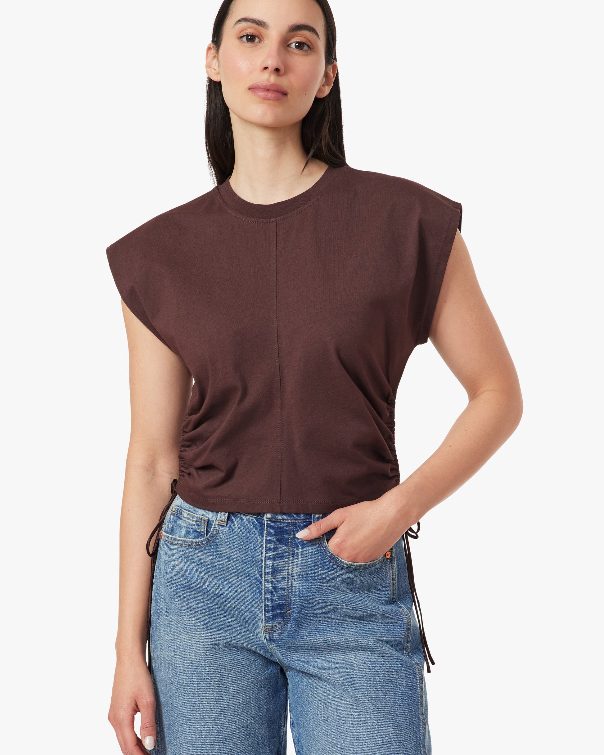 Woman wearing a brown sleeveless top and blue jeans on a white background