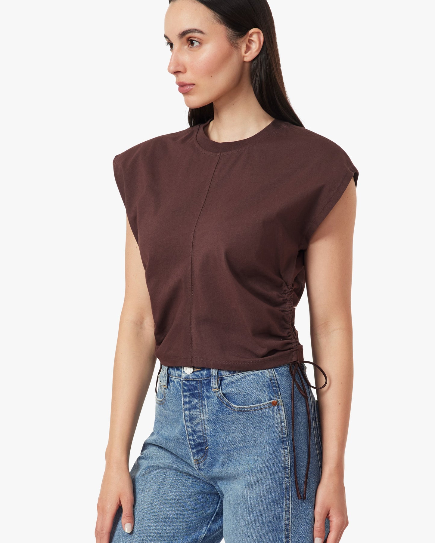 Woman wearing a brown sleeveless top and blue jeans on a white background