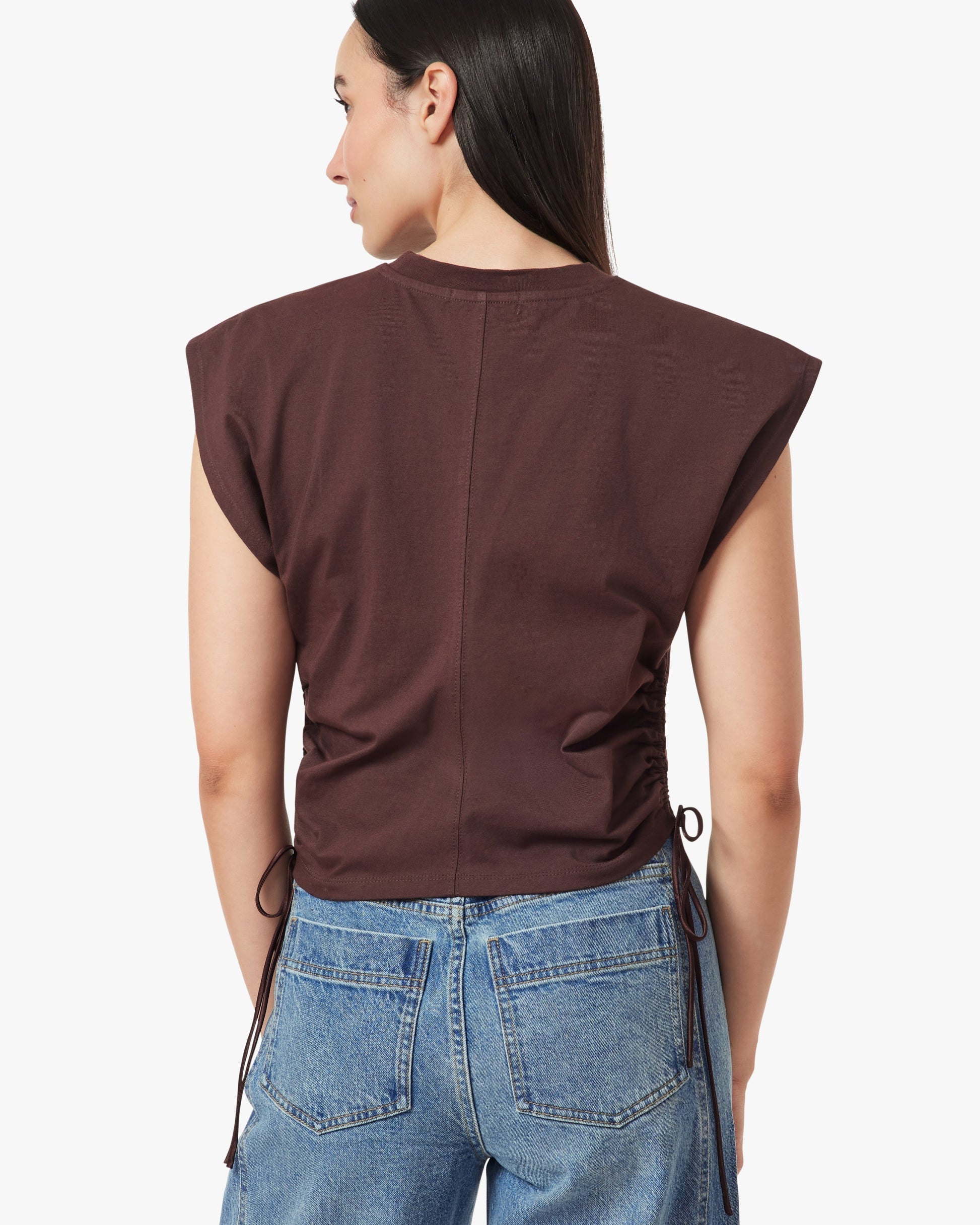 Person wearing a brown sleeveless top and blue jeans on a white background