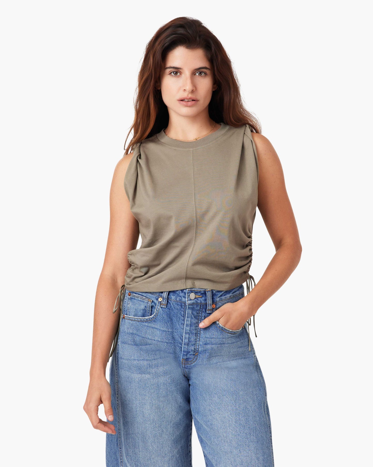 Woman wearing a sleeveless beige top and blue jeans on a white background