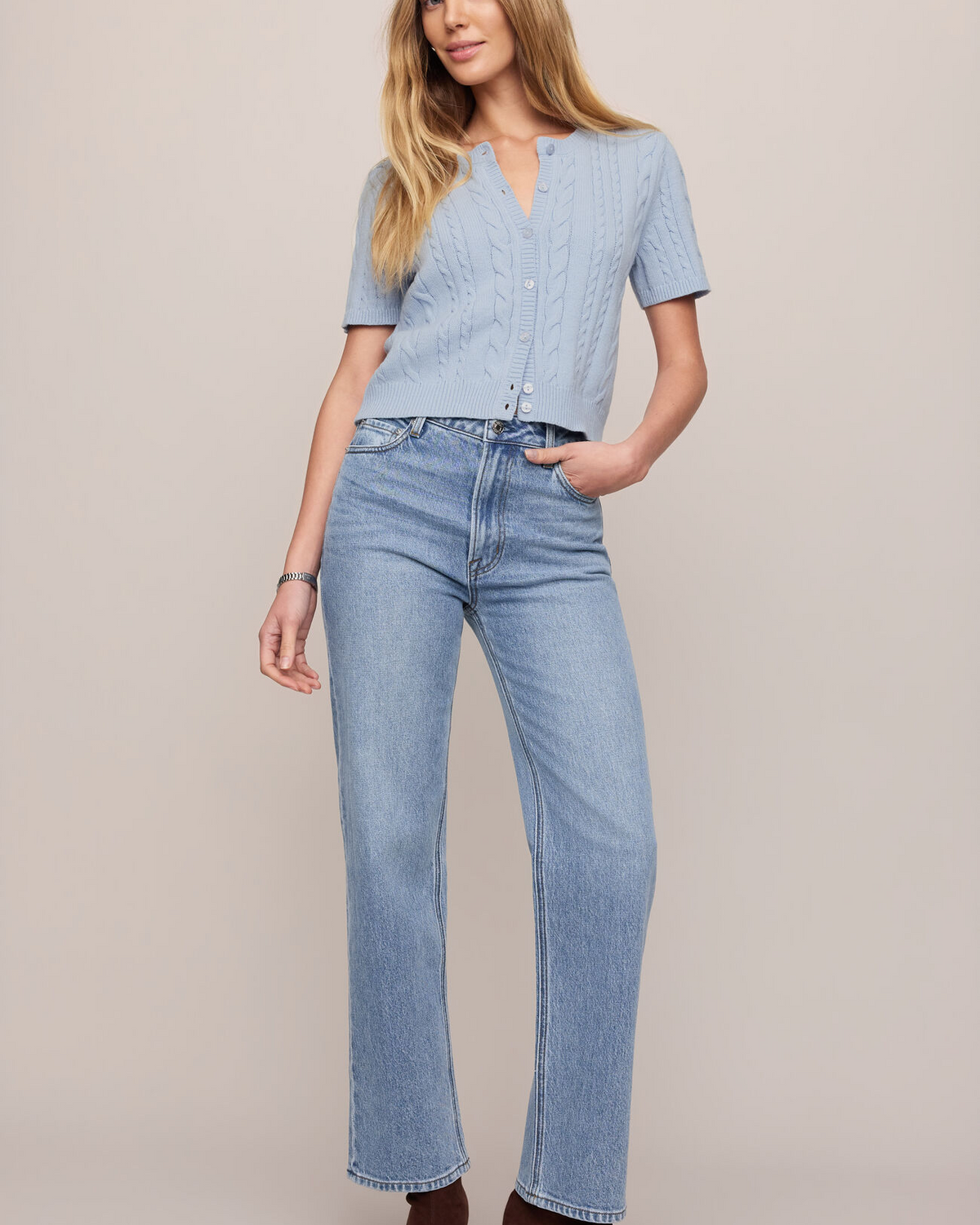 Woman wearing a light blue top and jeans on a plain background