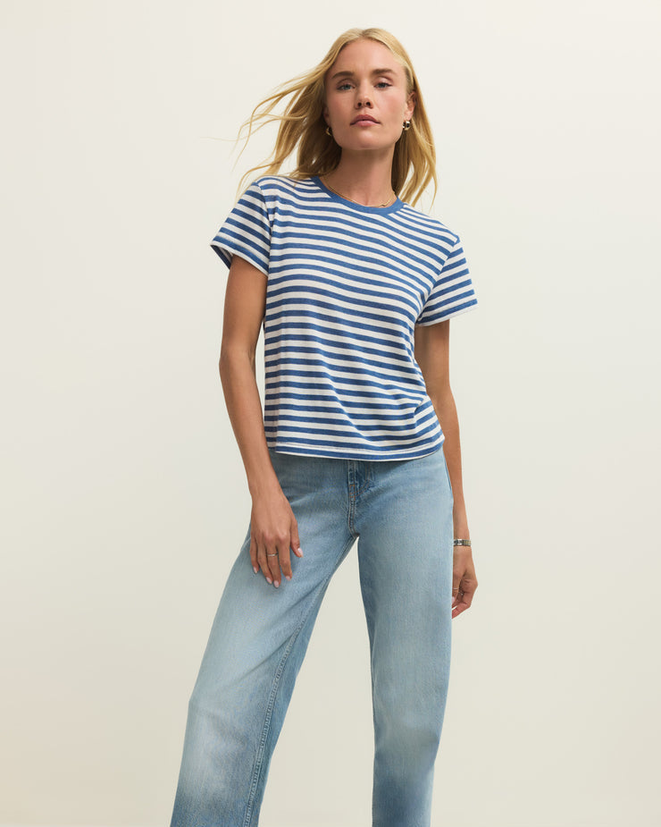 Woman wearing a blue and white striped t-shirt and light blue jeans on a plain background