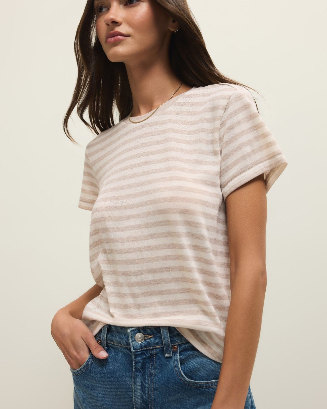 Woman wearing a striped shirt and blue jeans against a plain background