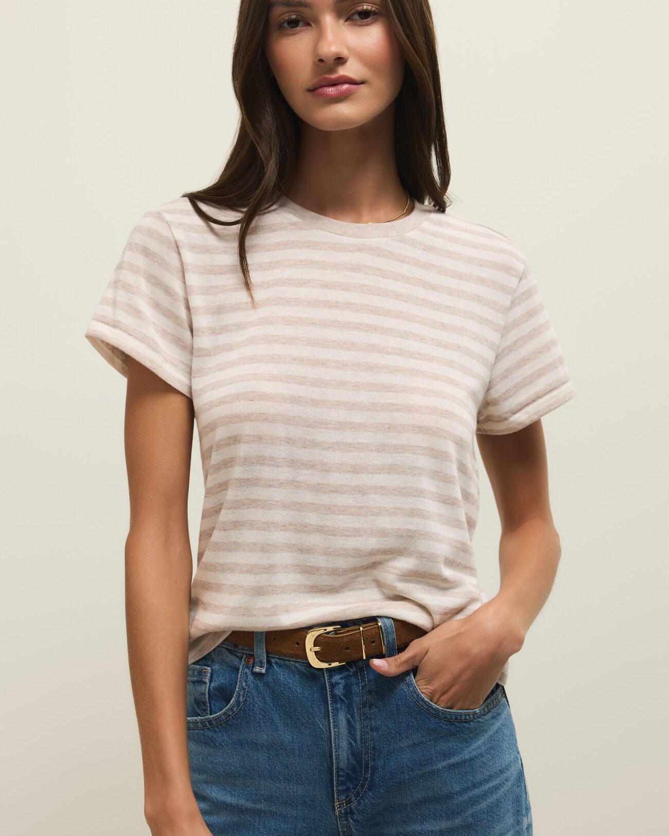 Woman wearing a striped shirt and blue jeans against a plain background