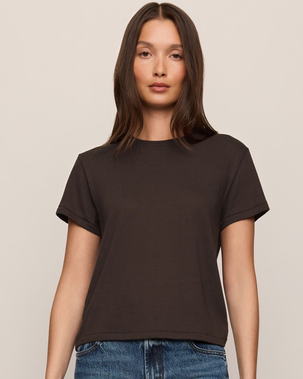 Woman wearing a black t-shirt and blue jeans against a beige background