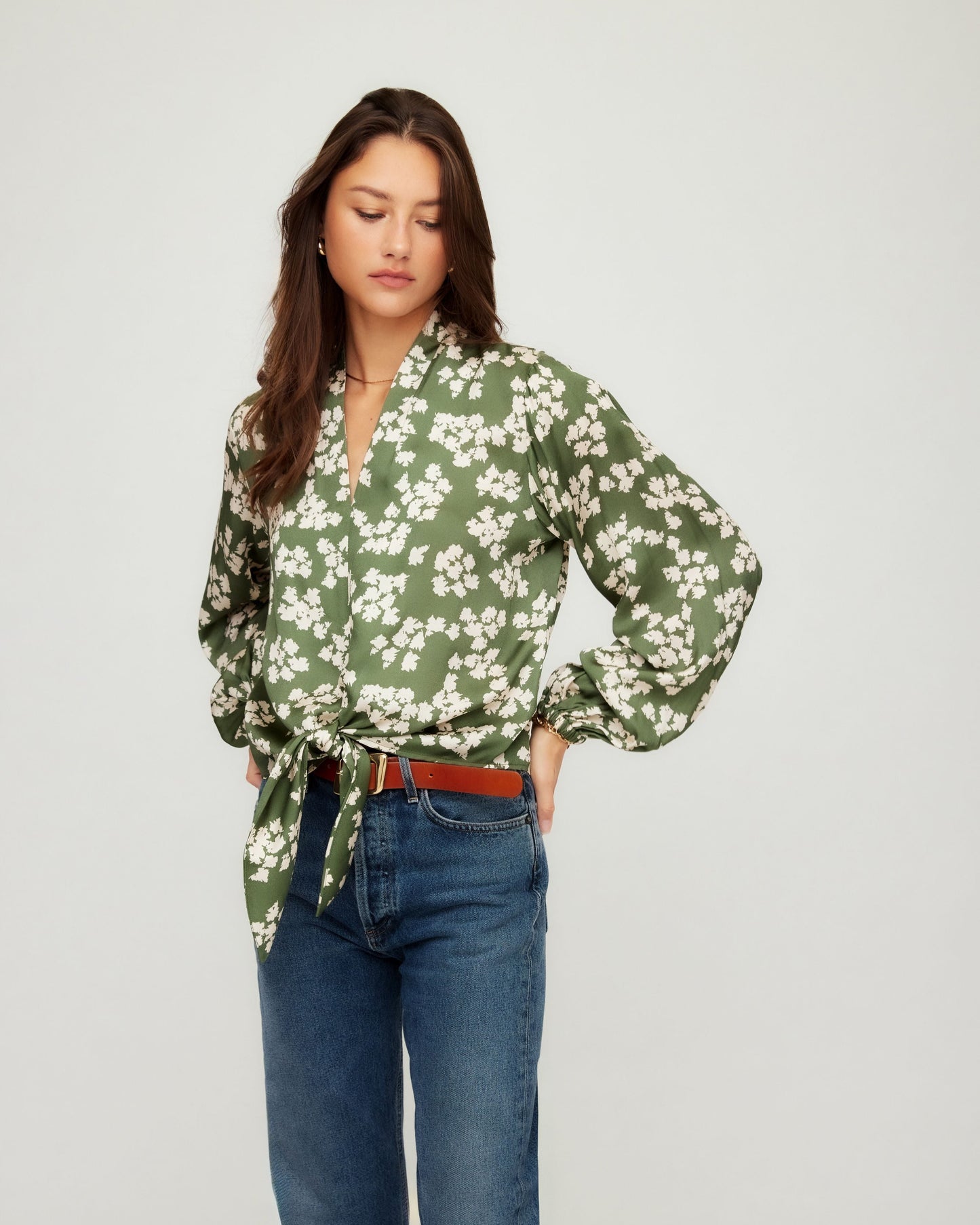 Woman wearing a green floral blouse and blue jeans on a white background