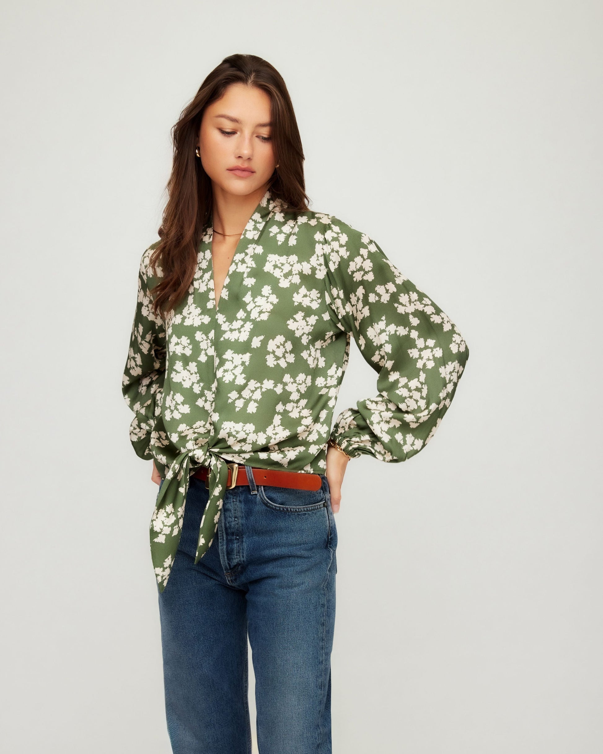 Woman wearing a green floral blouse and blue jeans on a white background