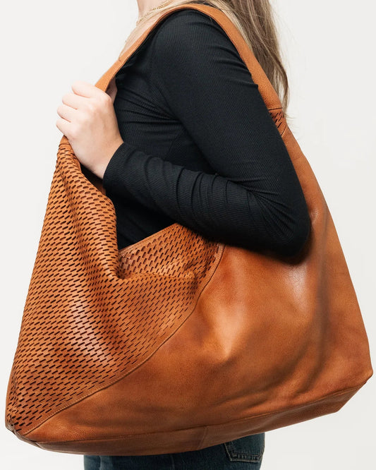 Person holding a brown leather handbag against a white background