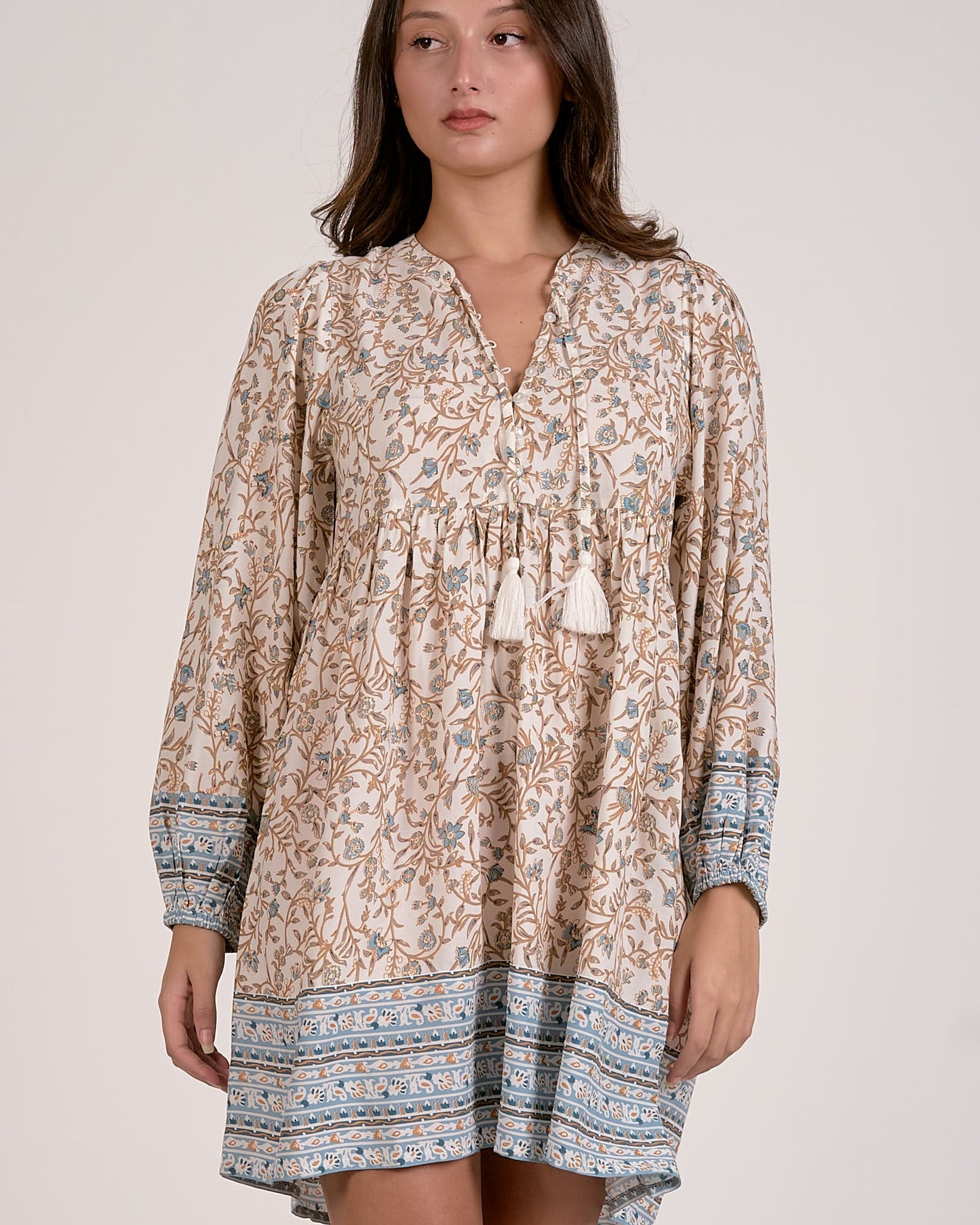 Woman wearing a patterned dress with tassels on a plain background