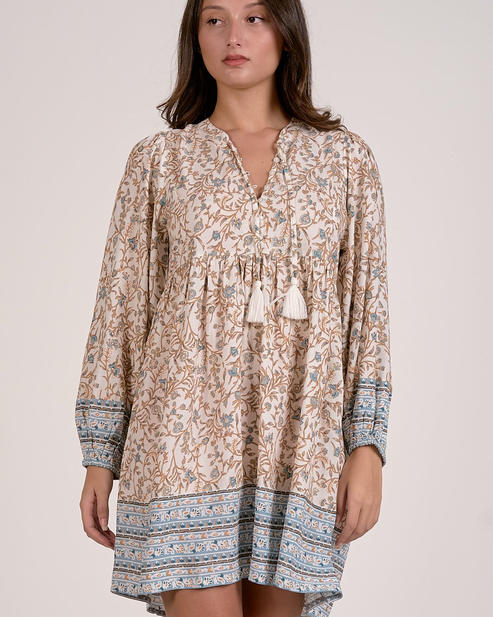 Woman wearing a patterned dress with tassels on a plain background