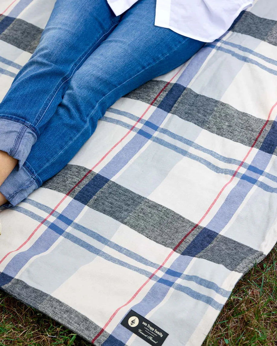 Person sitting on a plaid blanket with a visible brand label, wearing blue jeans and a white shirt.