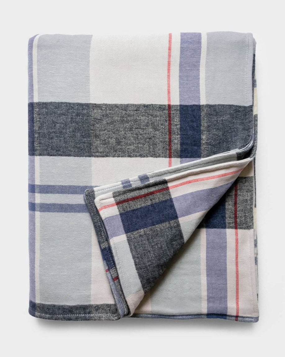 Folded plaid blanket with blue, white, and red colors on a light gray background