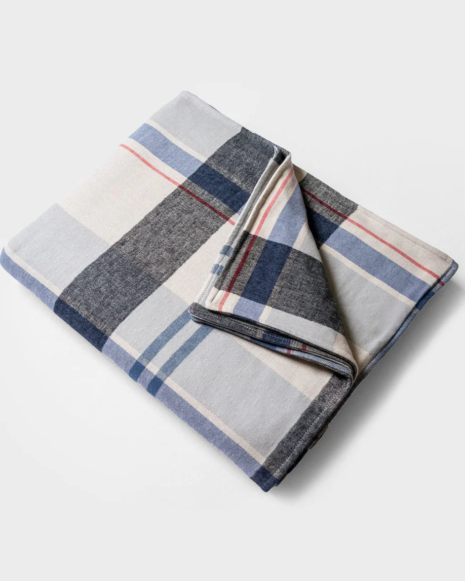 Folded plaid blanket with gray, blue, and red colors on a light gray background