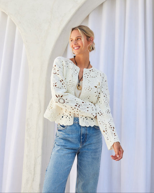 Woman wearing a white lace top and blue jeans standing in front of a white archway.