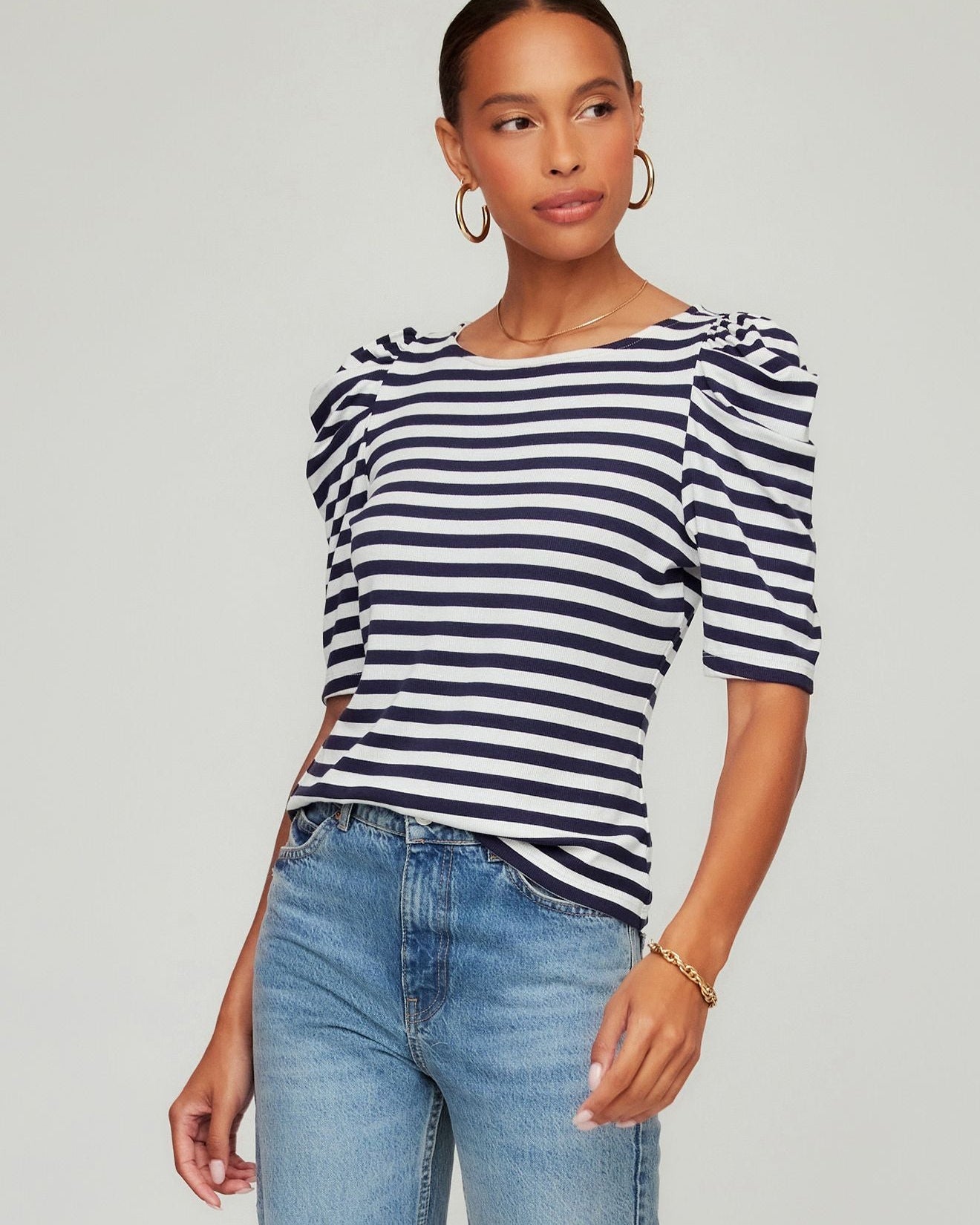 Woman wearing a navy and white striped top with blue jeans on a gray background