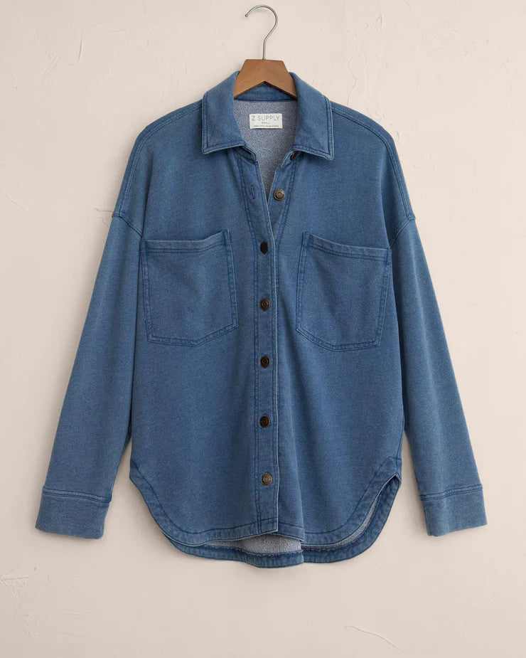 Blue denim shirt on a hanger against a beige background