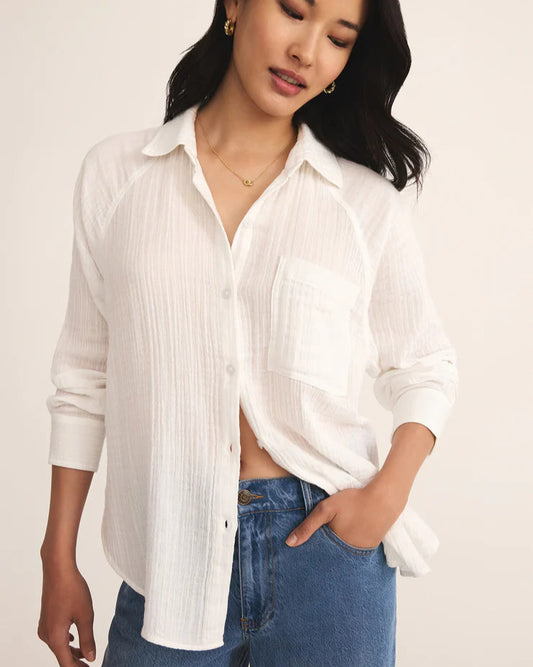 Woman wearing a white button-up shirt and blue jeans against a plain background