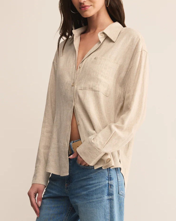 Woman wearing a beige button-up shirt and blue jeans against a plain background