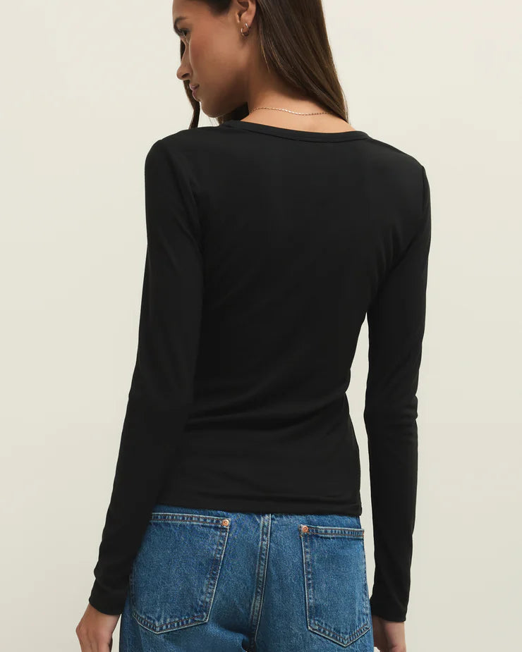 Person wearing a black long-sleeve top and blue jeans on a beige background