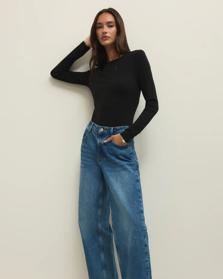 Woman wearing a black long-sleeve top and blue jeans against a white background