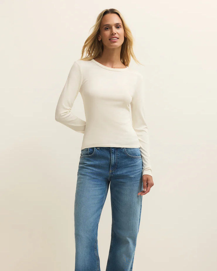 Woman wearing a white long-sleeve top and blue jeans on a white background